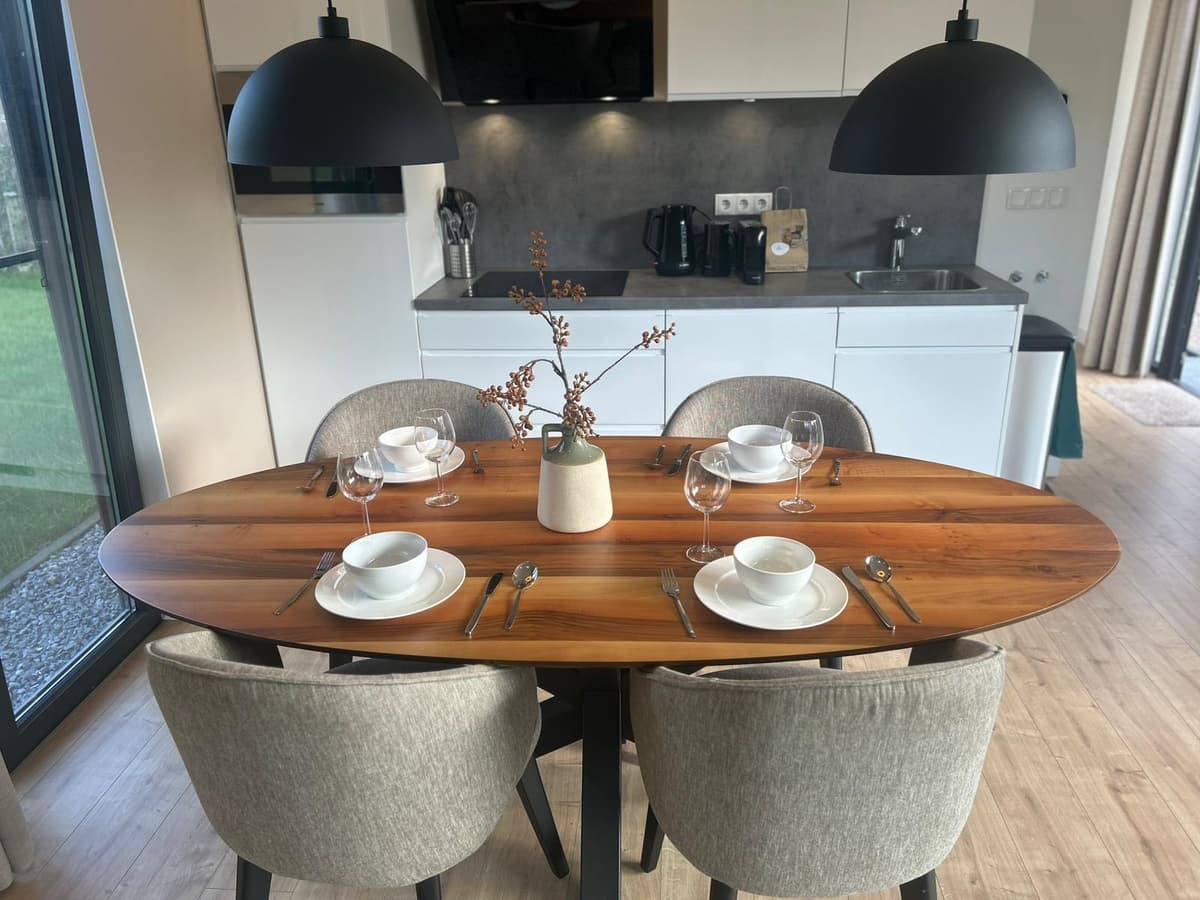 Eetkamer met een ovaal houten tafel, vier stoelen, en een moderne keuken op de achtergrond met witte kasten en apparatuur