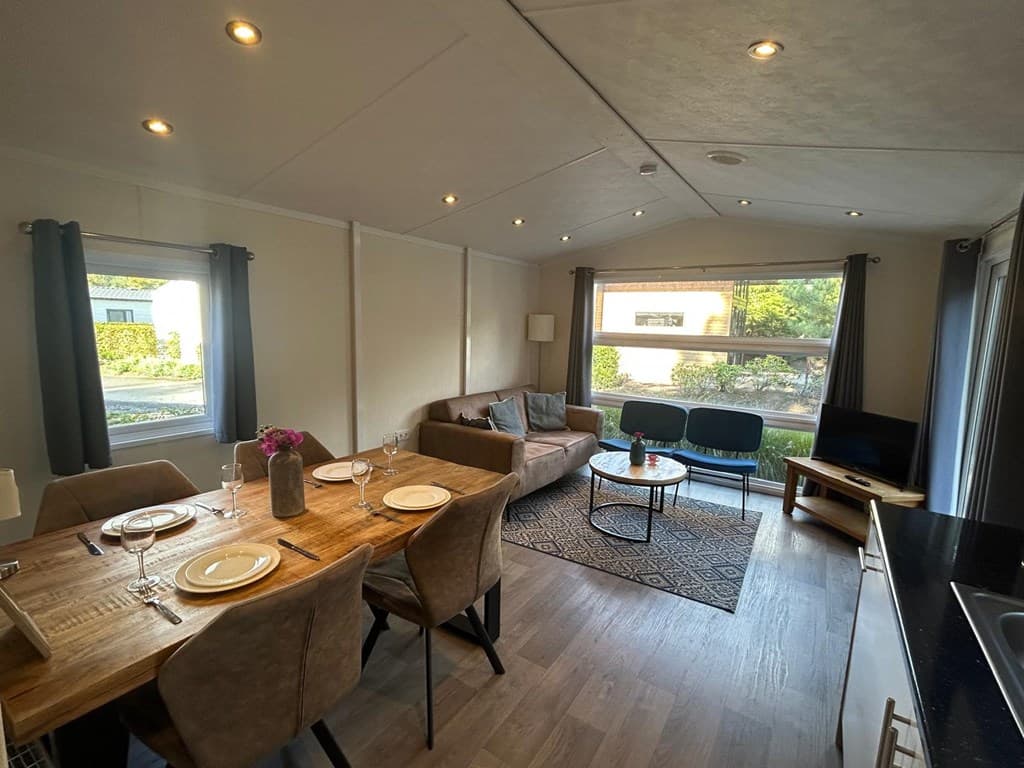 Woonkamer met eettafel, zithoek en grote ramen met uitzicht op buitenruimte