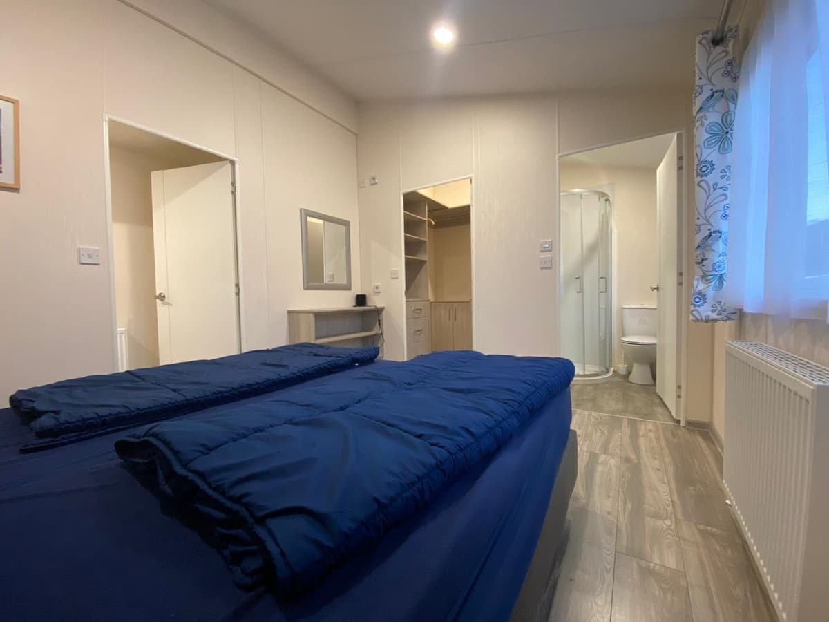 Slaapkamer met twee eenpersoonsbedden, kast, spiegel en toegang tot badkamer met douche en toilet.