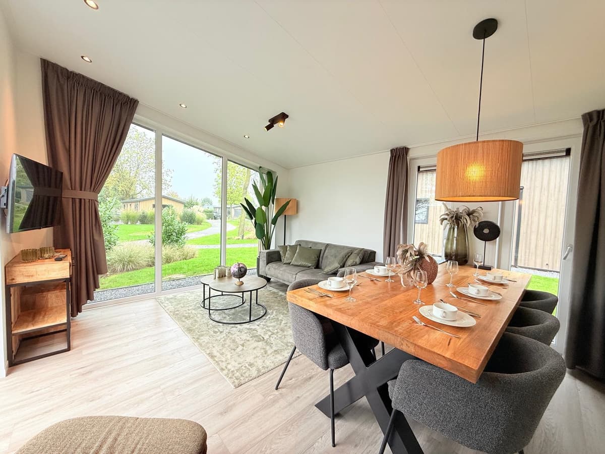 Moderne woonkamer met eettafel, bank en grote ramen met uitzicht op de tuin en omgeving