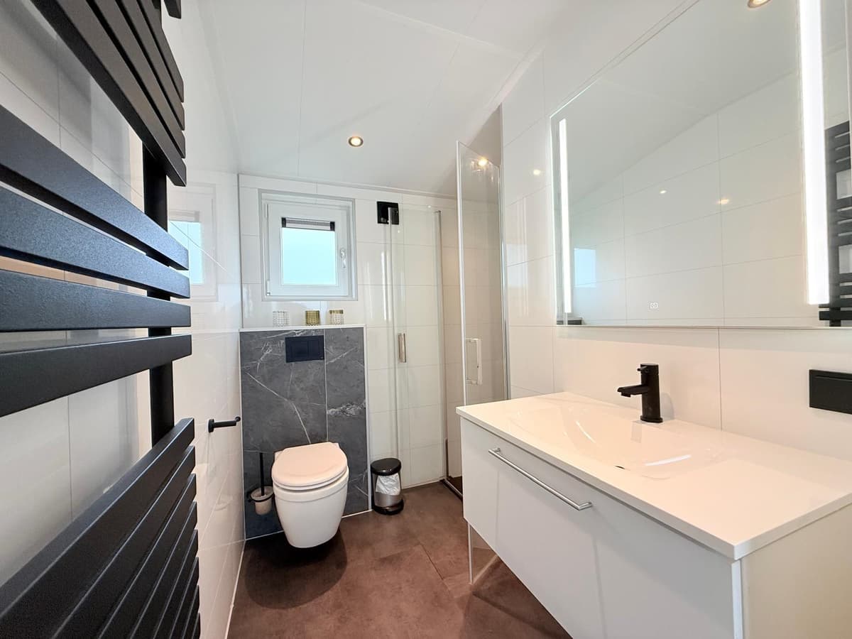 Moderne badkamer met toilet, inloopdouche, wastafel en grote spiegel, afgewerkt met lichte en donkere elementen