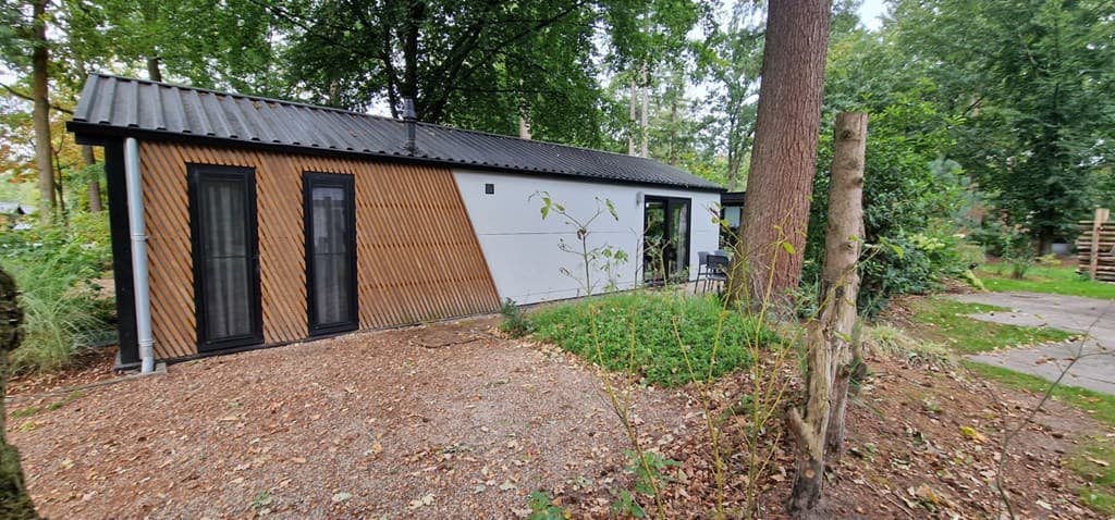 Moderne vakantiewoning met houten latten aan de gevel, omgeven door groen en een grindpad naar de ingang