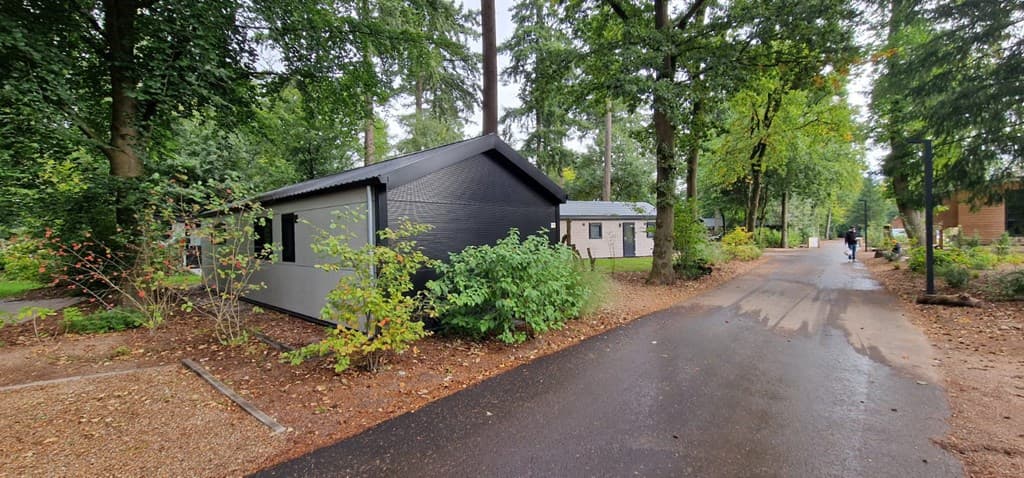 Moderne vakantiewoning omringd door bomen en planten, aan een geasfalteerd pad in EuroParcs Resort De Utrechtse Heuvelrug.