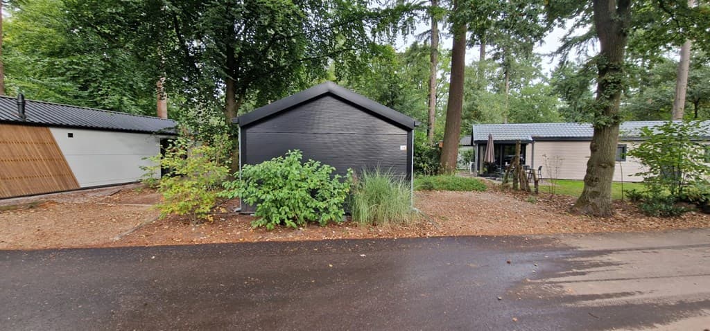 Zwart houten vakantiehuisje omringd door groen aan een rustige straat met bomen en andere woningen in de buurt