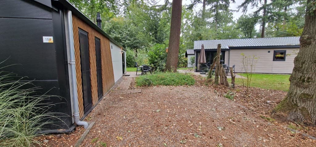 Zicht op een tuin met grindpad, bomen en nabijgelegen vakantiewoningen op EuroParcs Resort De Utrechtse Heuvelrug.