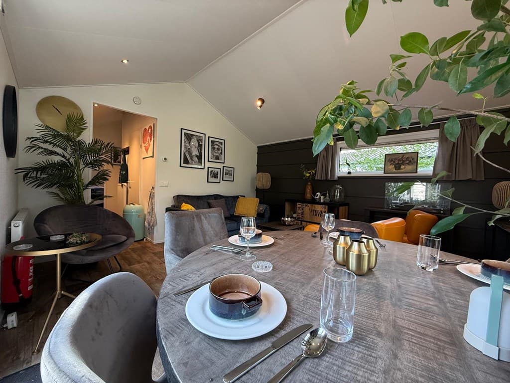 Huiskamer met eettafel, comfortabele stoelen en planten, zachte kleurstellingen en kunst aan de muren.