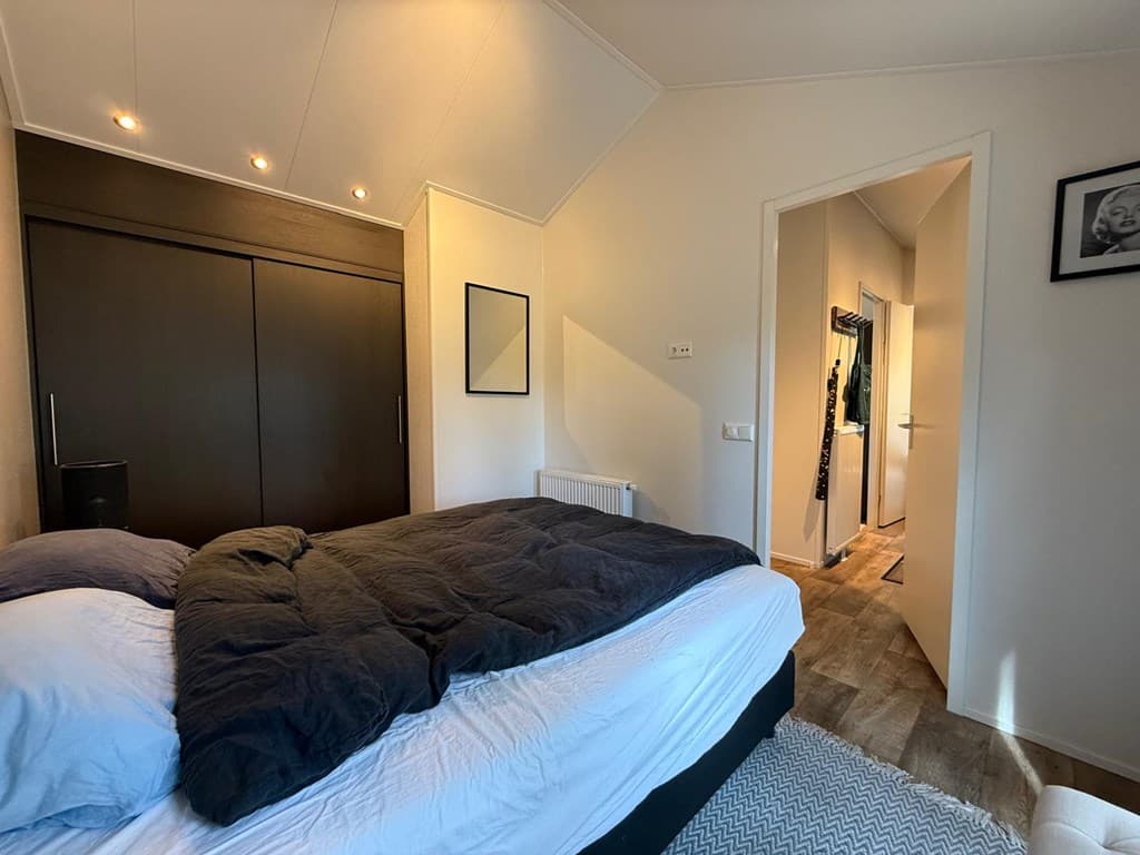 Slaapkamer met een tweepersoonsbed, inbouwkast en toegang tot een gang met deur naar andere ruimtes.