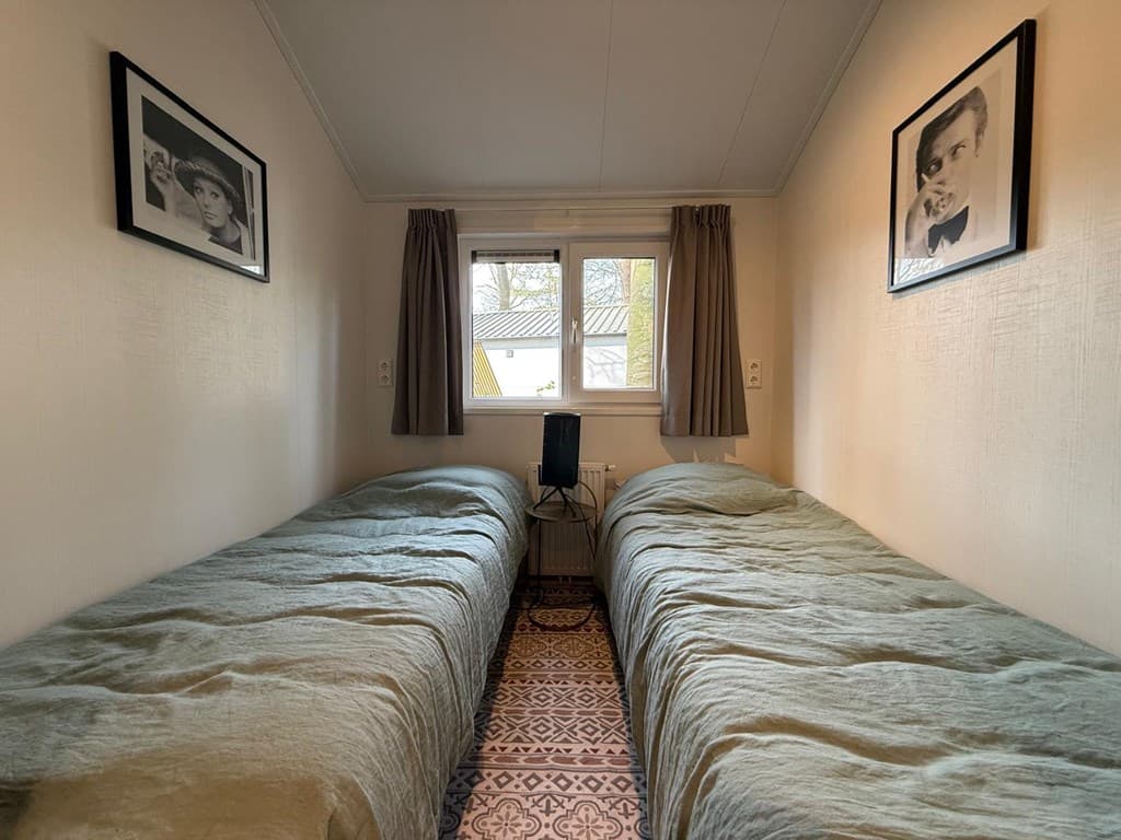 Slaapkamer met twee eenpersoonsbedden, ramen met gordijnen en zwart-wit foto's aan de wanden.