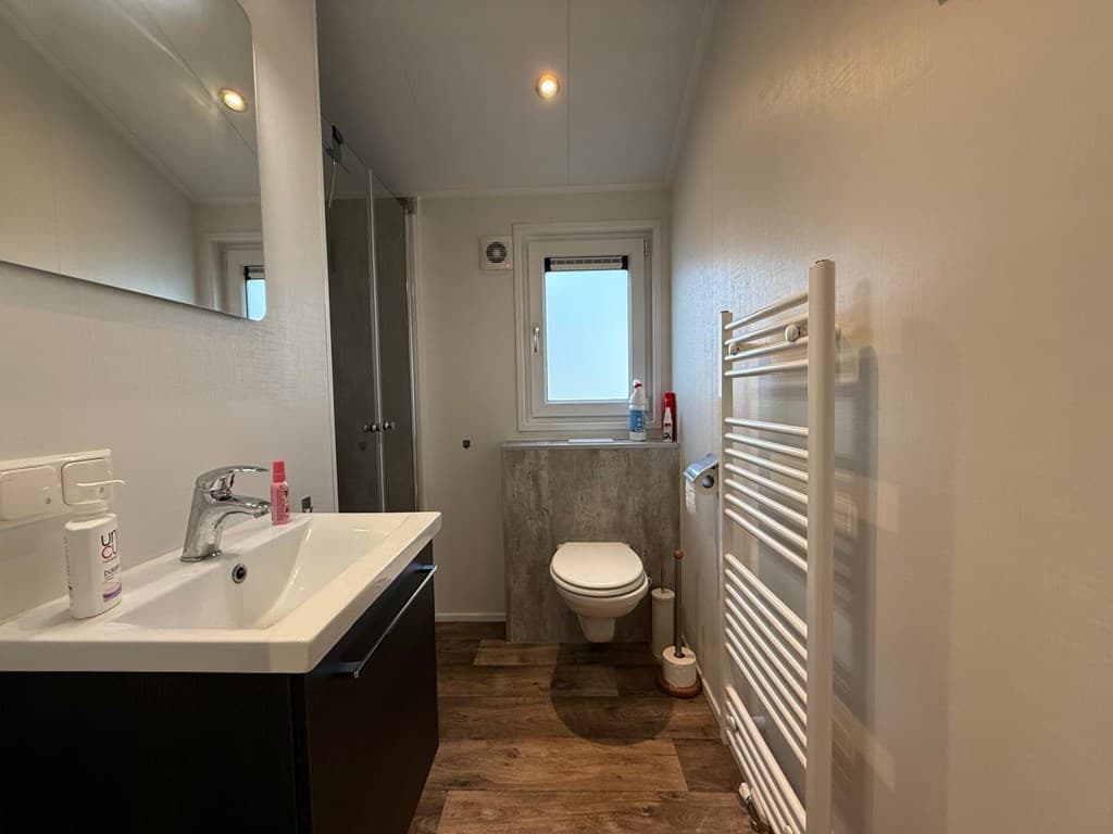 Moderne badkamer met wastafel, spiegel, toilet, handdoekenradiator en glazen douchecabine aan de muur