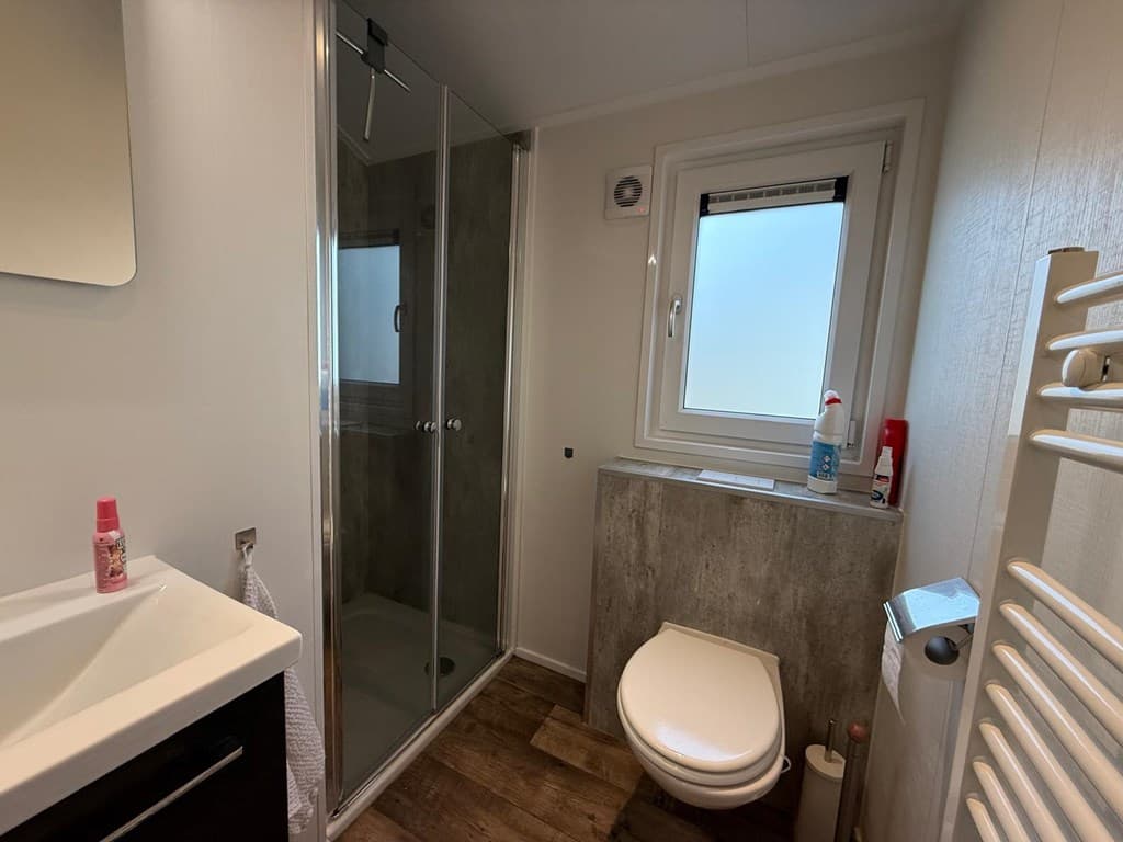 Moderne badkamer met douche, toilet en wastafel, lichtinval van een raam en houten vloerplanken