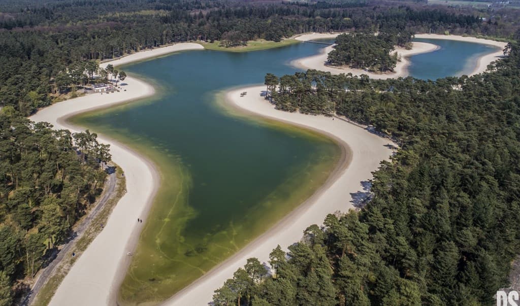 Luchtfoto van een uitgestrekt watergebied met zandstranden en groene bossen rondom, gelegen in EuroParcs Resort De Utrechtse 
