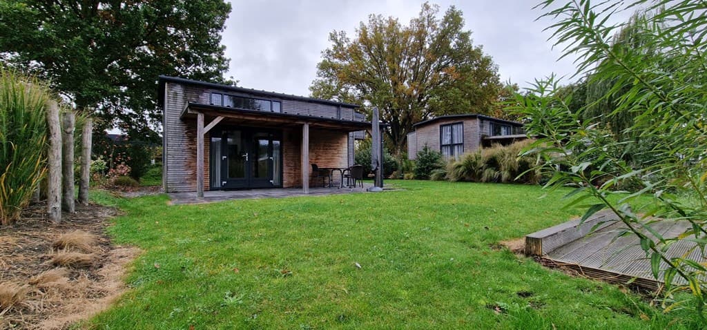 Moderne vakantiewoning met houtafwerking en overdekt terras, omringd door gras en groene begroeiing