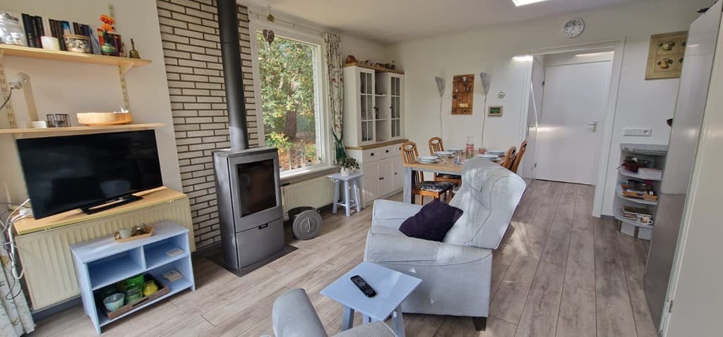 Woonkamer met een zitgedeelte, televisie, houtkachel en eettafel bij een vakantiehuis in Chaam
