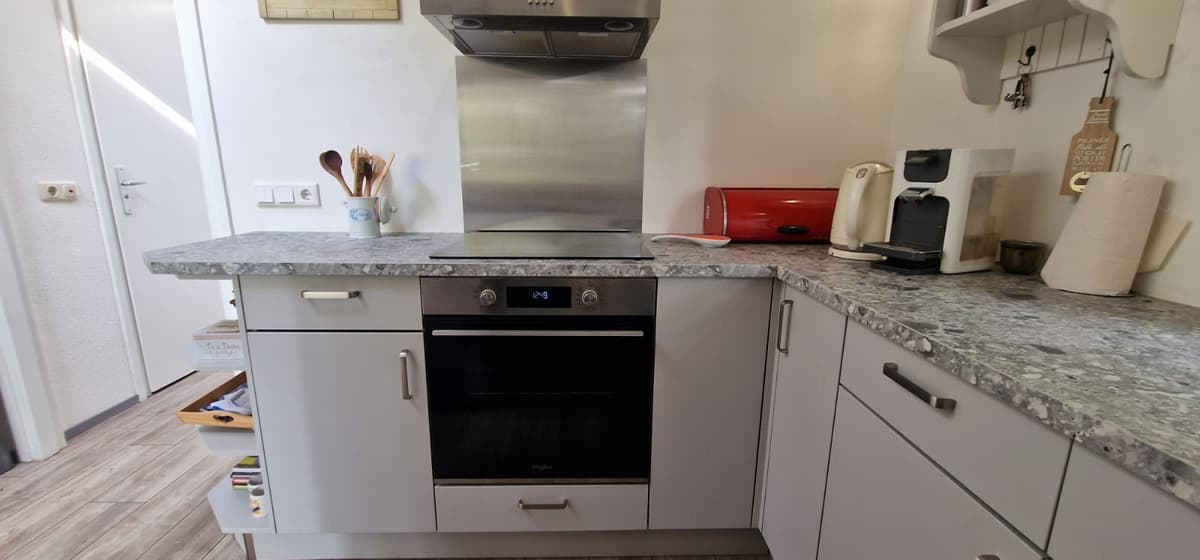 Moderne keuken met een steenachtige werkblad, ingebouwde oven en diverse keukenapparatuur in lichte kleuren.