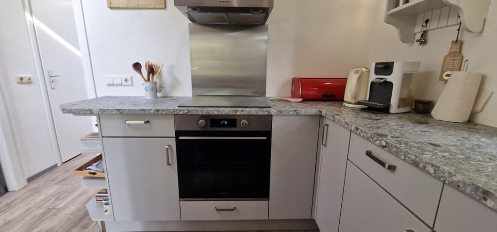 Moderne keuken met een steenachtige werkblad, ingebouwde oven en diverse keukenapparatuur in lichte kleuren.