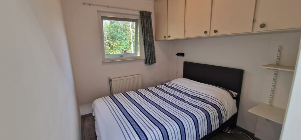 Kamer met een tweepersoonsbed, kledingkasten en een raam met uitzicht op groen.