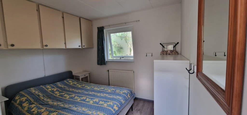 Slaapkamer met een tweepersoonsbed, kledingkasten en een raam met uitzicht op groen.