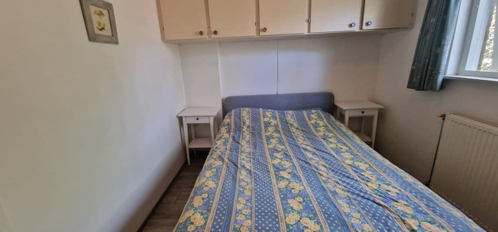 Slaapkamer met een éénpersoonsbed, nachtkastjes en kasten aan de muur, voorzien van een raam met groen uitzicht.