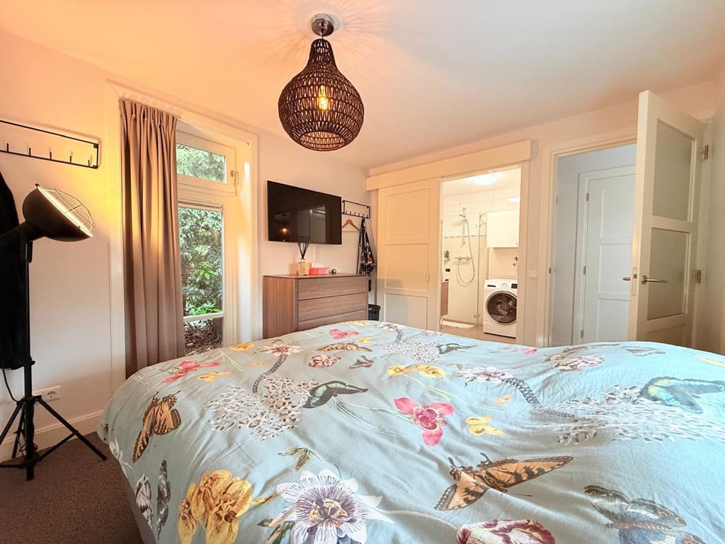 Sfeervolle slaapkamer met een groot bed, TV, kast en open deur naar een badkamer met wasmachine.