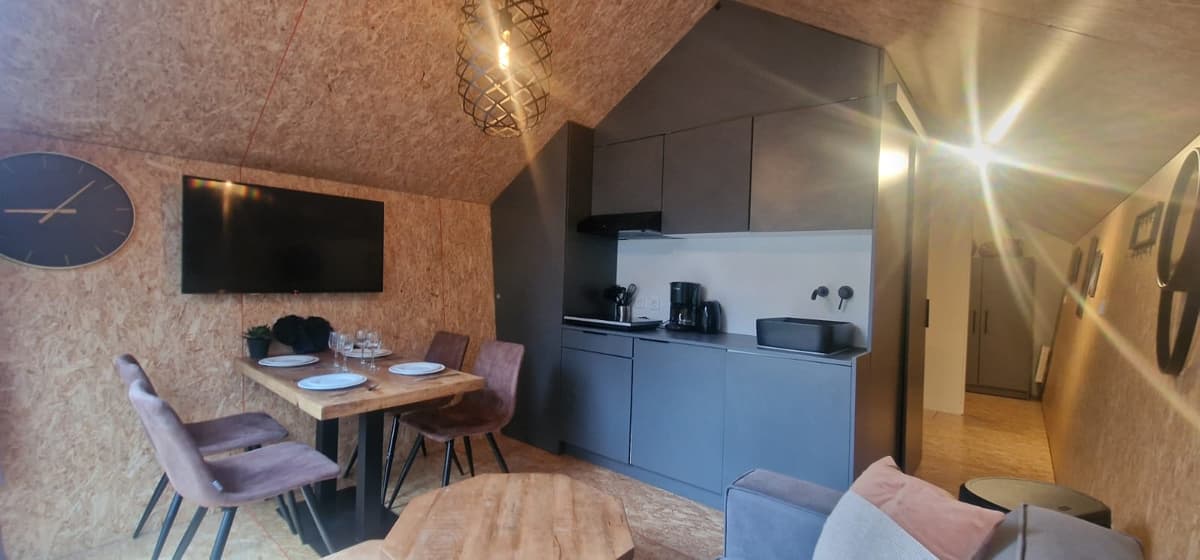 Gezellige woonkamer met open keuken, eettafel, moderne meubels en grote tv met wandklok aan de muur