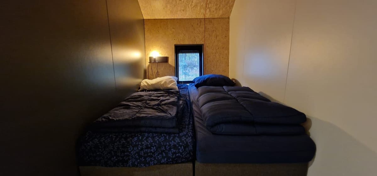 Tweepersoons slaapkamer met twee afzonderlijke bedden en een klein raam voor natuurlijk licht