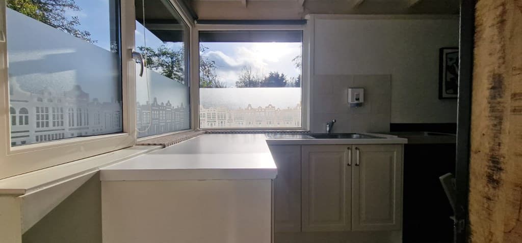 Keuken met een werkblad en raam dat uitkijkt op een tuin met zicht op bomen en de lucht.