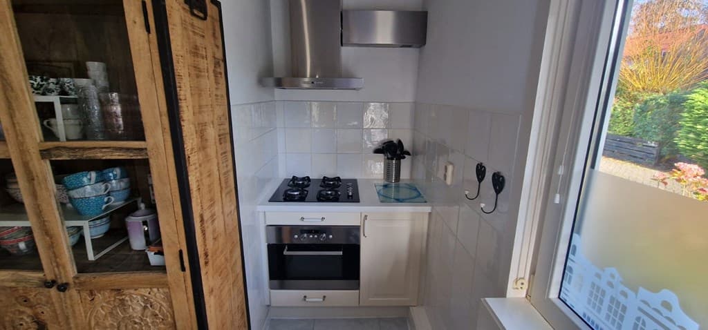 Keuken met een gasfornuis, oven, afzuigkap en een kast met servies in een lichte ruimte