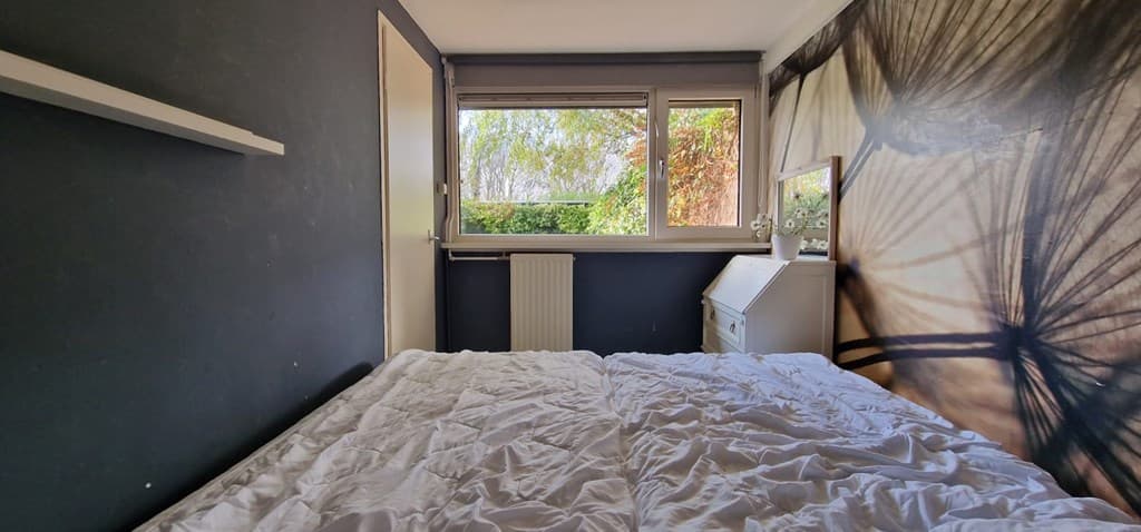 Slaapkamer met een bed, bureau, venster met uitzicht op groen, en een wand met een natuurlijke print.