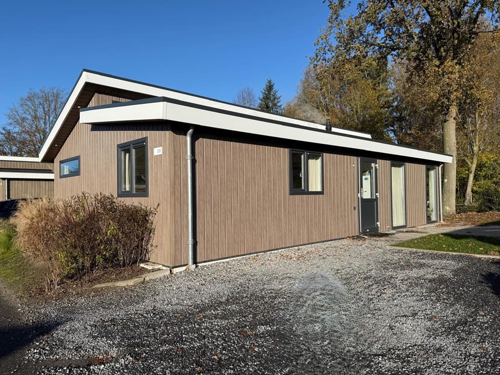 Vakantiehuis met houten gevel, moderne uitstraling, grote ramen en doorgang naar de voordeur, omgeven door gras en bomen