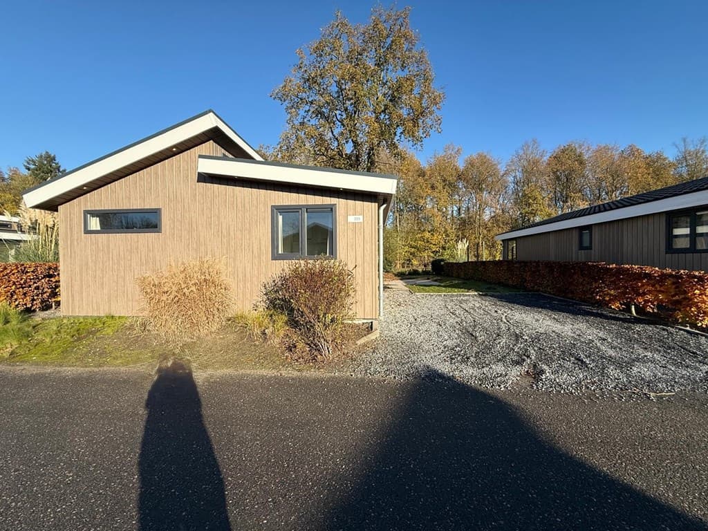 Vakantiehuis met houten gevel en enkele ramen, omringd door een grindpad en groene begroeiing in EuroParcs Zuiderzee.