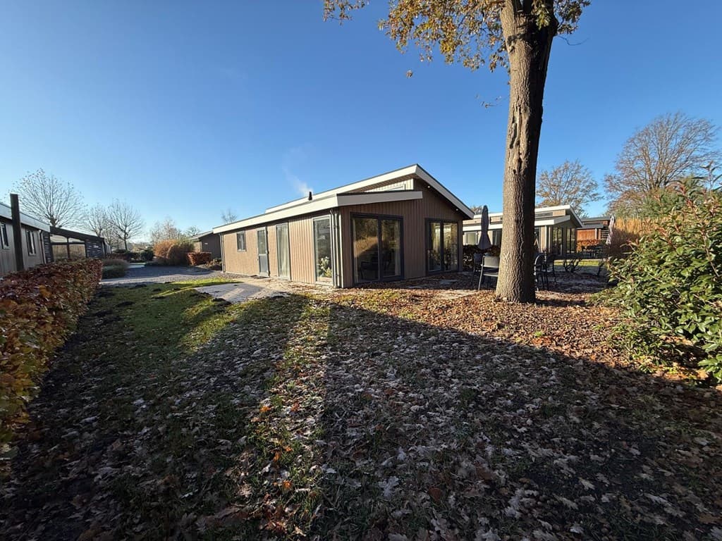 Moderne vakantiewoning omgeven door een tuin met herfstbladeren en bomen, locatie EuroParcs Zuiderzee.