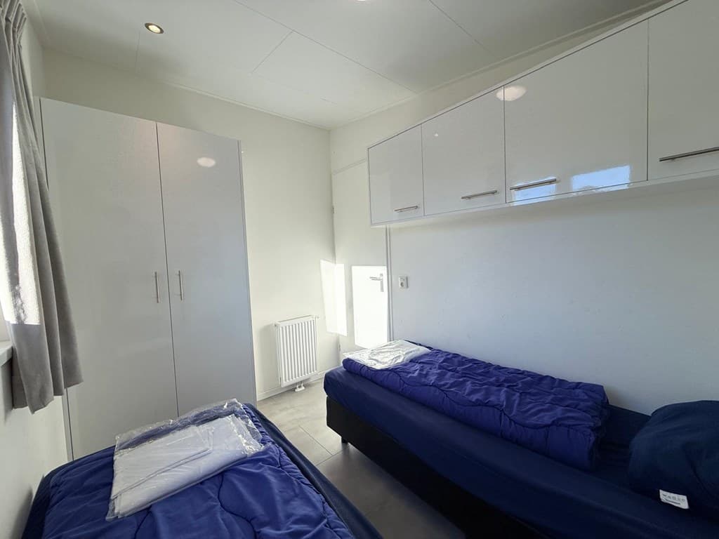 Slaapkamer met lichte muren, twee enkele bedden met dekbedden en een witte kast aan de wand.