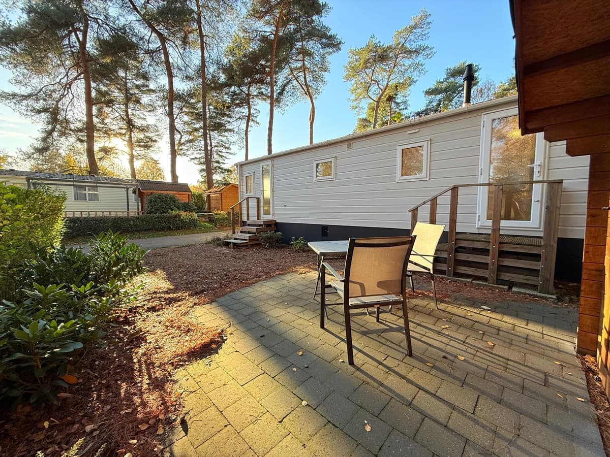 Terras met zitmeubelen, omgeven door groen, met een mobiele woning en bomen op de achtergrond