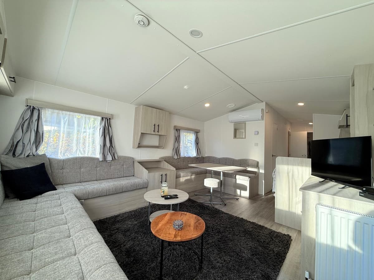 Moderne woonkamer met zithoek, eettafel en kitchenette in lichte tinten, grote ramen zorgen voor natuurlijk licht