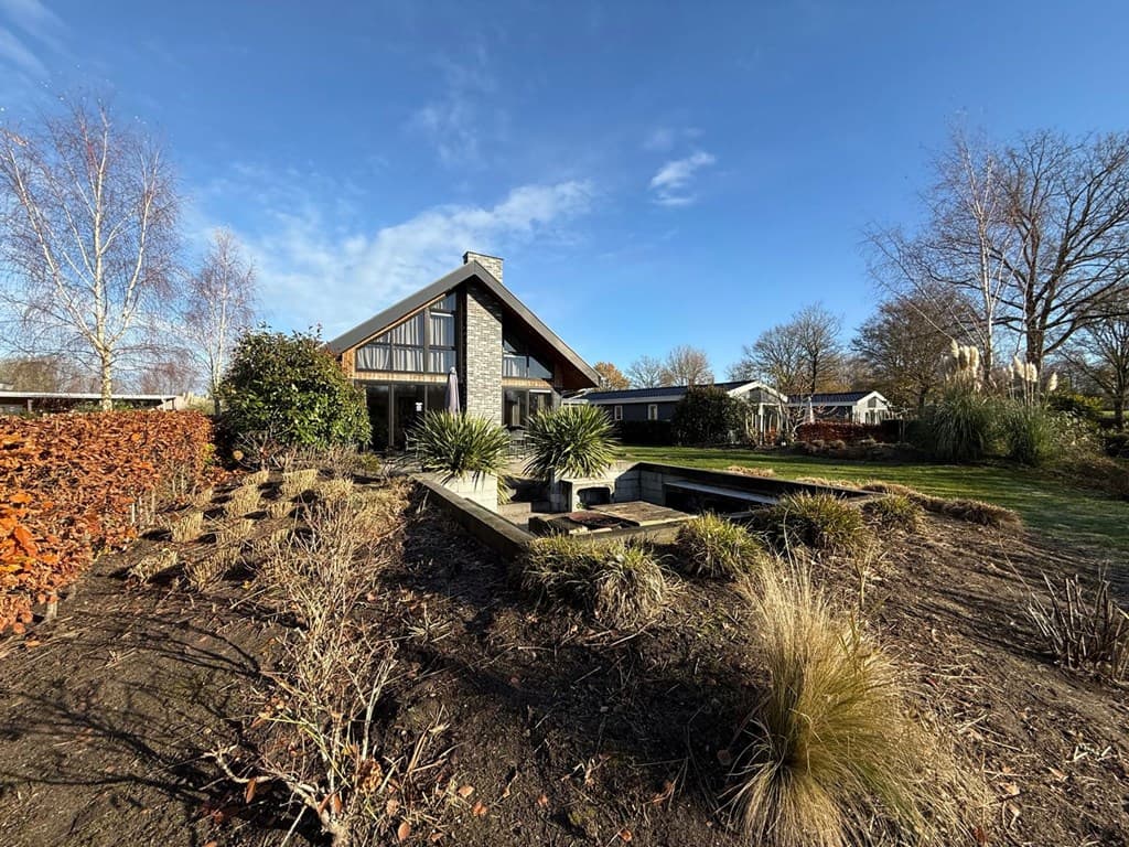 Moderne vakantiewoning met een tuin, vijver en groene beplanting onder een blauwe lucht in EuroParcs Zuiderzee.