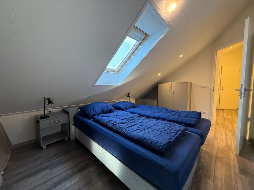 Slaapkamer met twee eenpersoonsbedden, nachtkastjes en een dakkapel met raam. Moderne inrichting en lichte wanden.