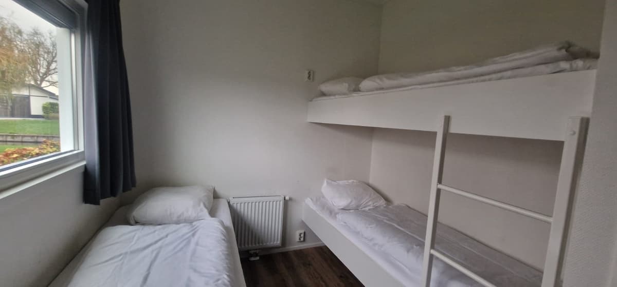 Slaapkamer met een eenpersoonsbed en een stapelbed, een raam met gordijnen en een radiator aan de muur.