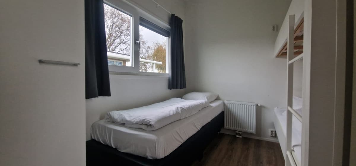 Slaapkamer met een eenpersoonsbed, gordijnen en kast, lichte muren en een radiator