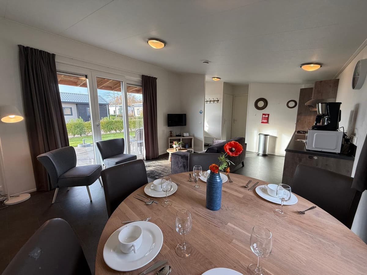 Eetruimte met houten tafel, stoelen, bank, televisie en toegang tot buitenruimte met een uitzicht op het groen