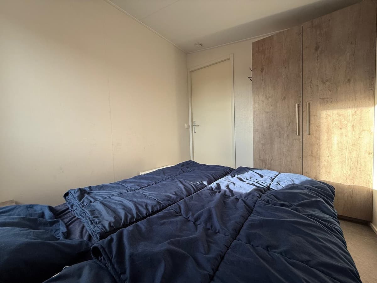 Slaapkamer met twee eenpersoonsbedden en een kast, natuurlijk licht van een raam aan de rechterkant.