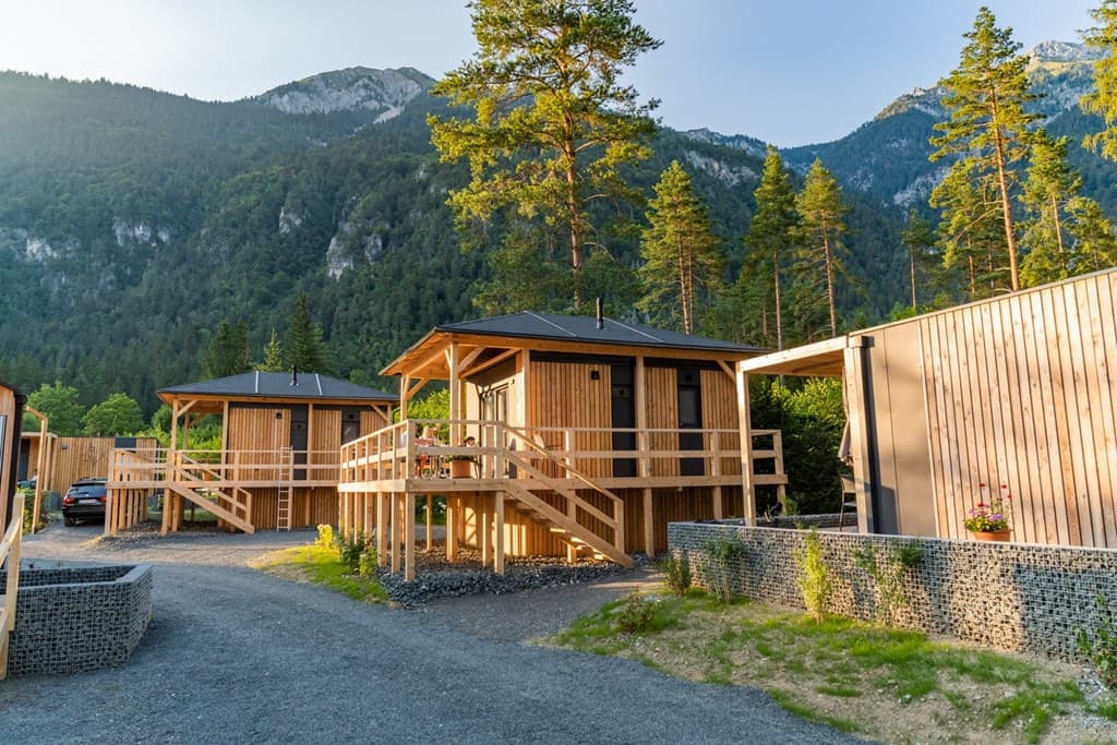 Prefab vakantiewoningen met houten veranda's en omringd door bomen, gelegen in een bergachtig landschap.
