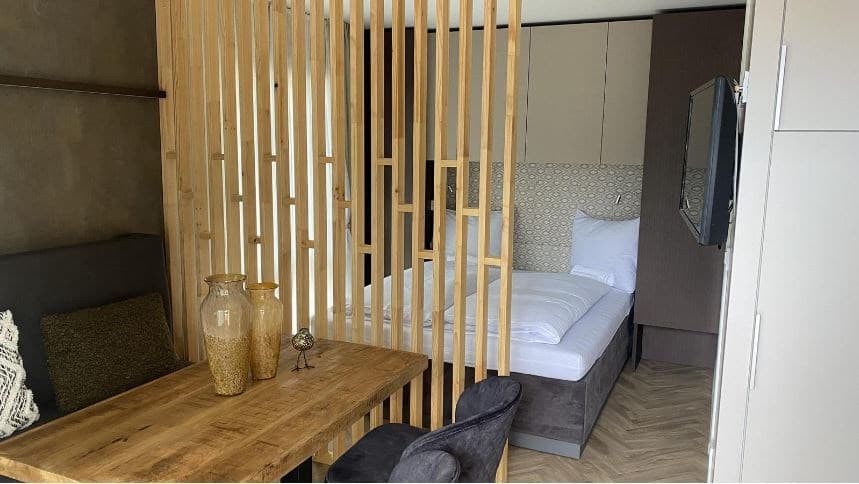 Slaapkamer met houten afscheiding, bed, tafel met vazen en televisie op de wand, moderne inrichting en warme kleuren.