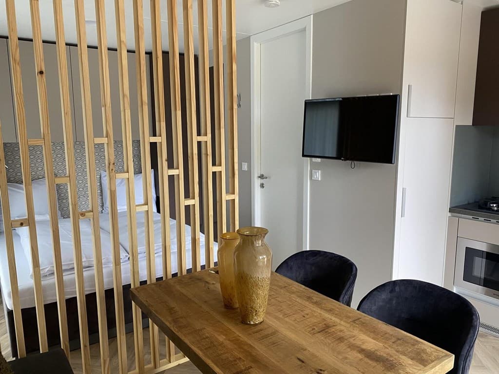 Moderne woonkamer met eettafel, stoelen, keuken, en bed achter een houten scheidingswand