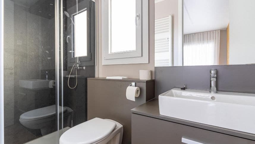 Moderne badkamer met douche, wastafel en toilet in neutrale kleuren, groot raam voor natuurlijk licht