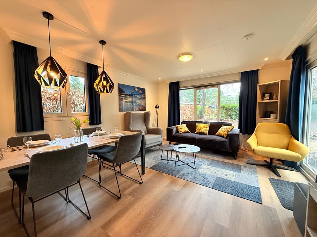 Gezellige woonkamer met eettafel, moderne stoelen, bank, kunst en zicht op buiten via grote ramen.