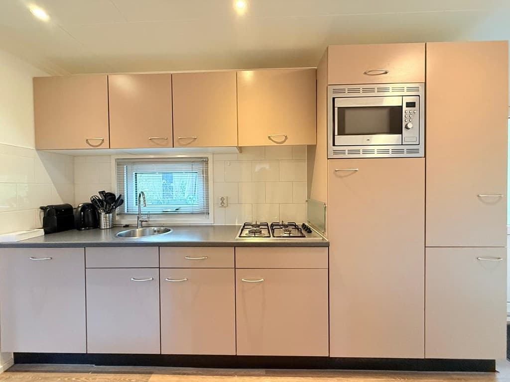 Moderne keuken met lichtroze kastjes, gasfornuis en een inbouwoven, afgewerkt met een kunststof werkblad.