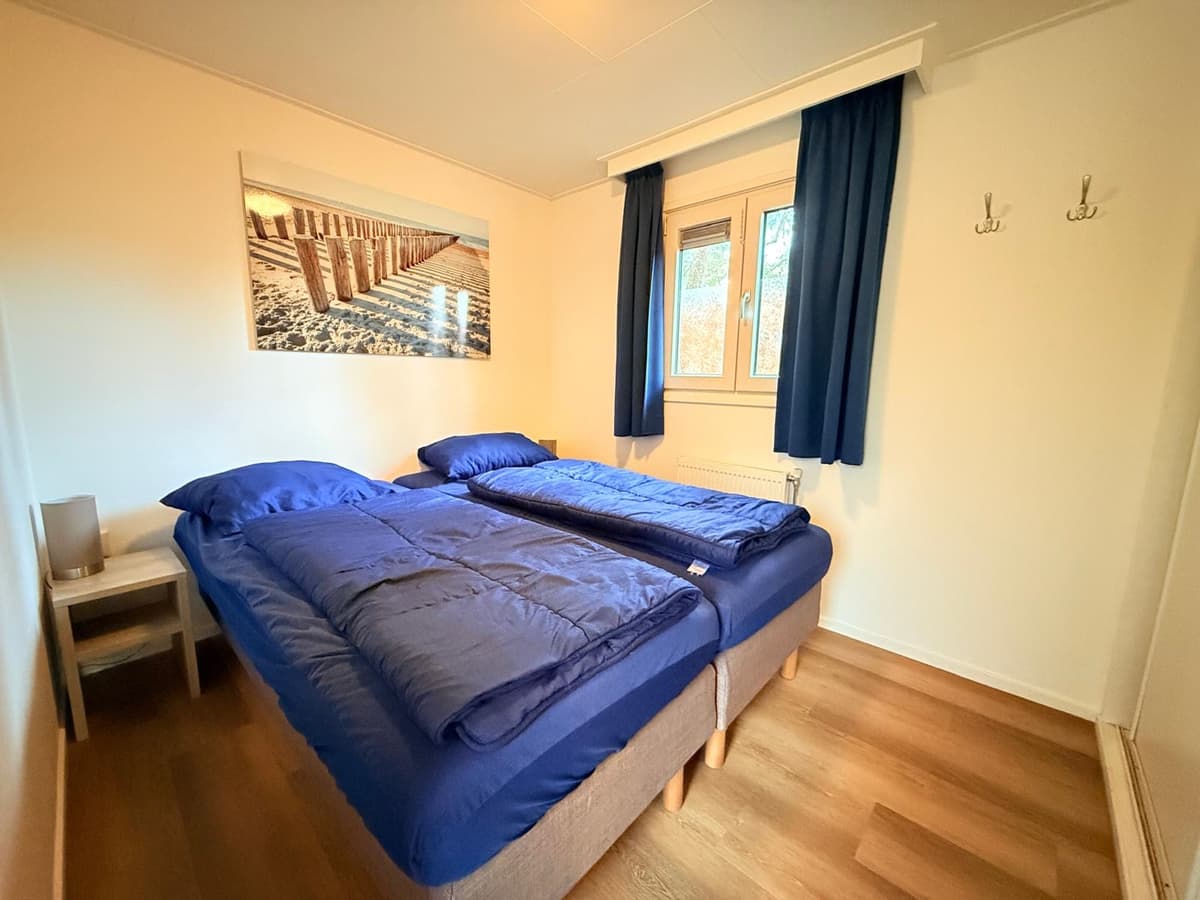 Slaapkamer met twee éénpersoonsbedden, houten vloer en raam met donkerblauwe gordijnen.