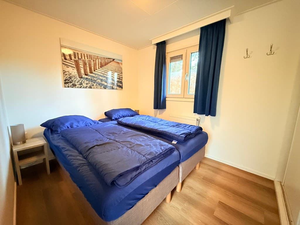 Slaapkamer met twee éénpersoonsbedden, houten vloer en raam met donkerblauwe gordijnen.