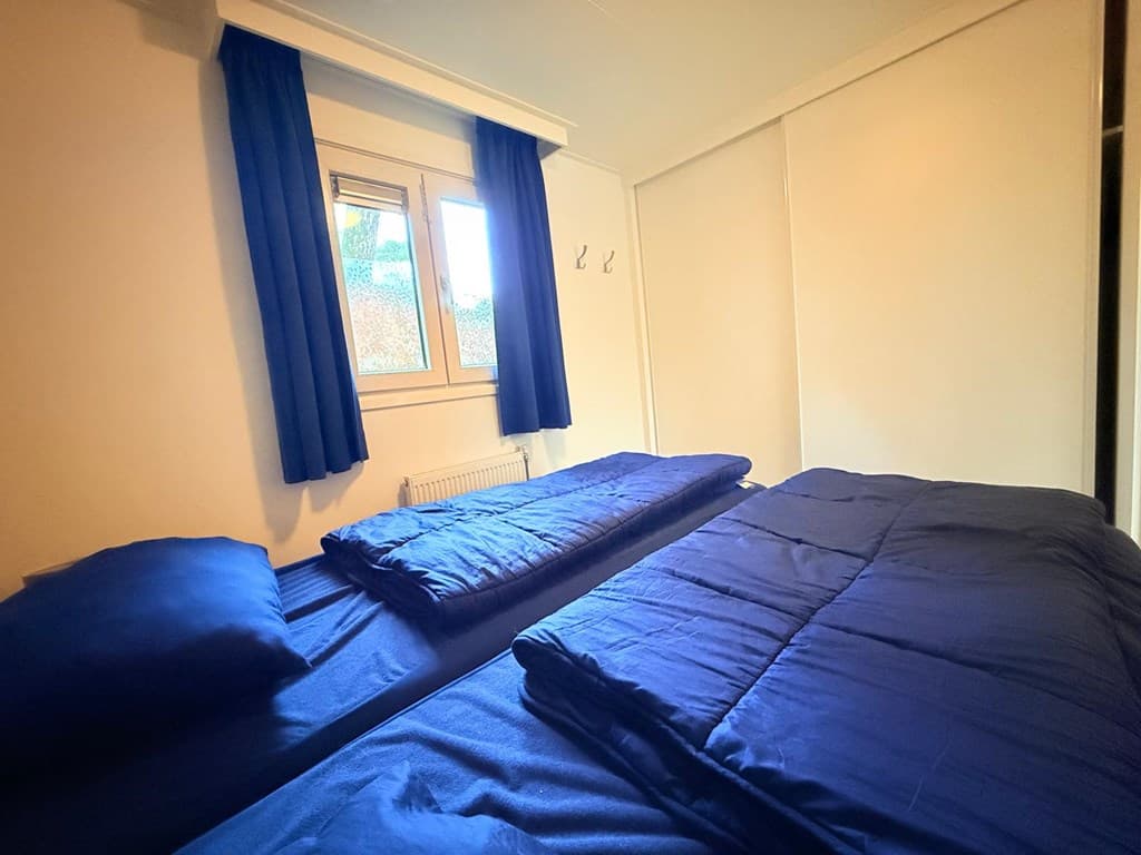 Slaapkamer met twee losse bedden, blauwe dekbedden en een raam met blauwe gordijnen.