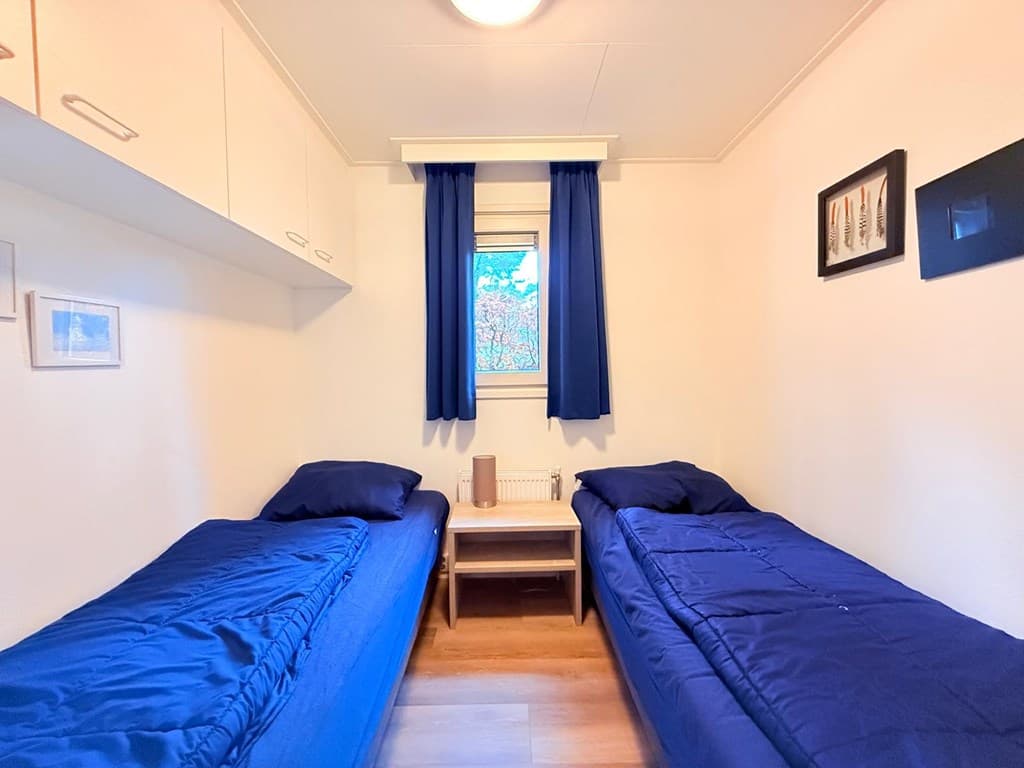 Slaapkamer met twee eenpersoonsbedden, een wandkast en een klein nachttafeltje bij een raam met blauwe gordijnen